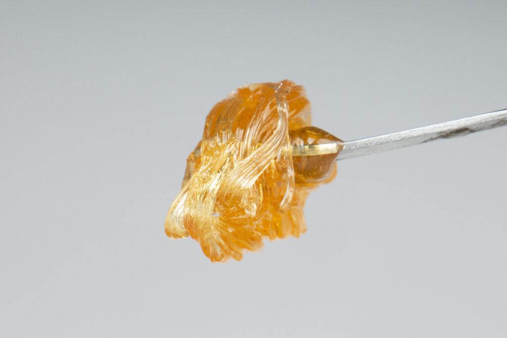 yellow gold cannabis extract wax concentrate dripping from the dabbing tool closeup.